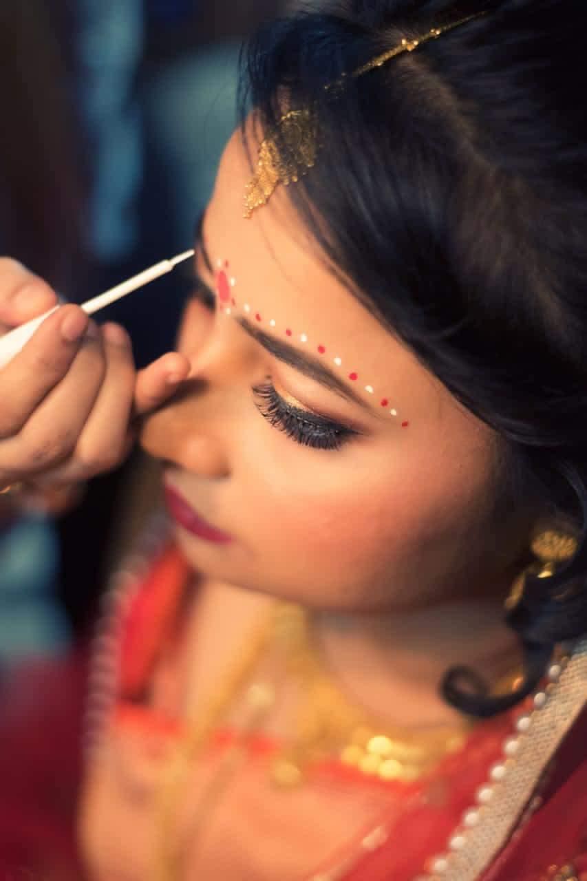 Hand-painting traditional chandan detailing on a Bengali bride — precision taught in class