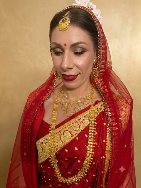 Bengali bridal look in crimson banarasi with layered gold jewellery on gold backdrop