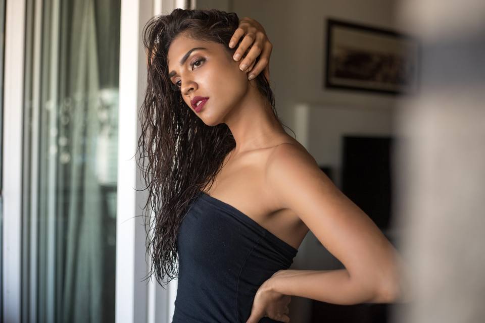 Editorial portrait by a window with wet-look hair and a black wrap